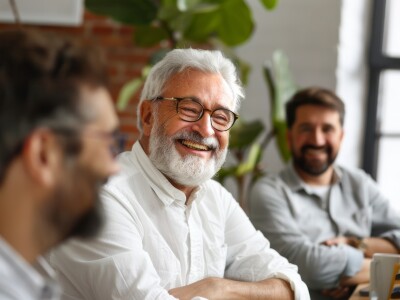 Portrait of senior businessman in office with colleagues in the background.