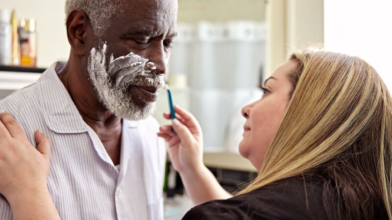 woman shaving face of older man