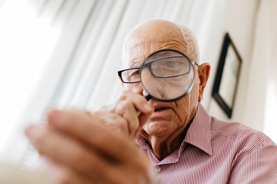 Retired senior male looking through magnifying glass at fossil